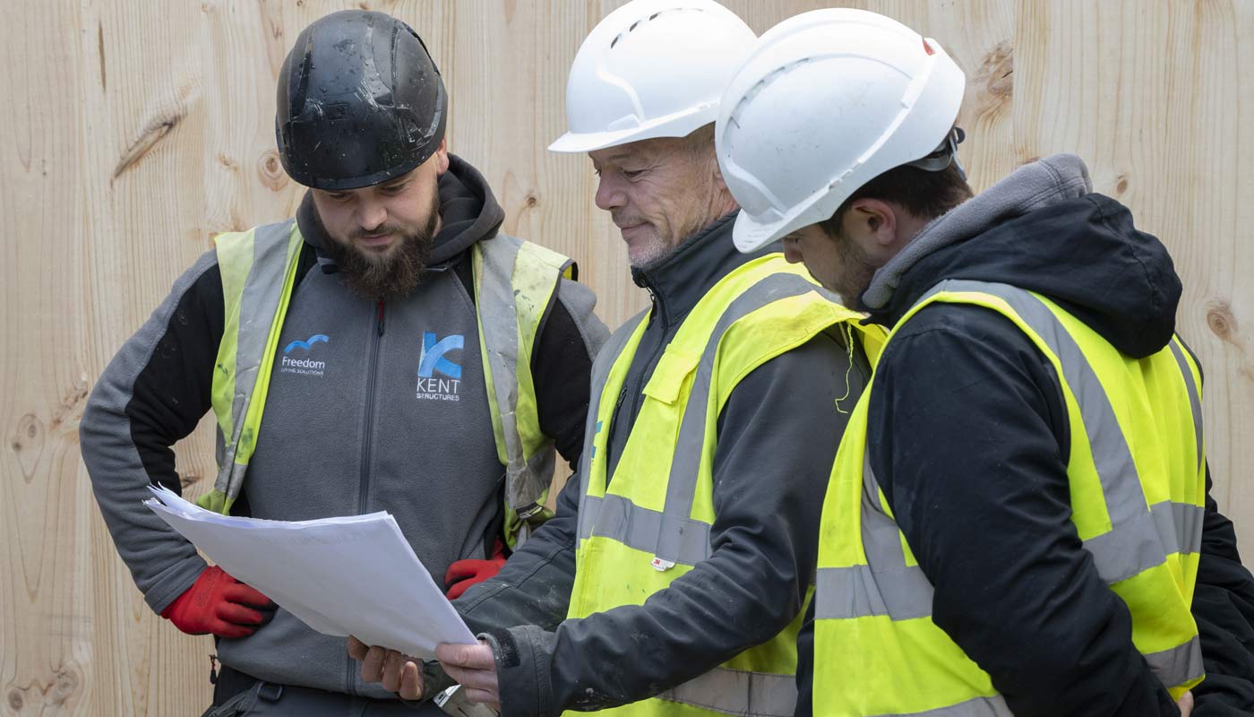Architect and site workers in hard hats on a construction site reviewing value engineered plan.
